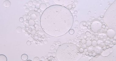 Yumuşak, soyut güzellik arka planında, temiz bir kozmetik dokusu yaratmak için hafif ışıkla aydınlatılmış, berrak sıvı içinde yüzen yağ kabarcıkları var..