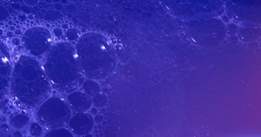 Temiz bir kozmetik doku yaratmak için koyu mavi ışıkla aydınlatılmış, berrak sıvı içinde yüzen narin yağ kabarcıkları olan, soyut güzellik arka planı..