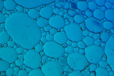 Temiz bir kozmetik doku yaratmak için mavi ışıkla aydınlatılmış, berrak sıvı içinde yüzen narin yağ kabarcıkları olan, soyut güzellik arka planı..