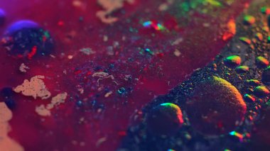 Yağlı sıvının renkli soyut boşanmaları neon kırmızı, mavi ve yeşil renklerde. Kabarcıklar, lekeler ve ışıldayan doku parlak bir fütüristik arkaplan yaratır.