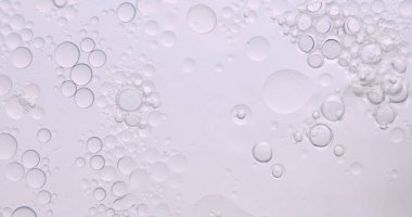 Yumuşak, soyut güzellik arka planında, temiz bir kozmetik dokusu yaratmak için hafif ışıkla aydınlatılmış, berrak sıvı içinde yüzen yağ kabarcıkları var..