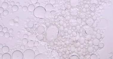 Yumuşak, soyut güzellik arka planında, temiz bir kozmetik dokusu yaratmak için hafif ışıkla aydınlatılmış, berrak sıvı içinde yüzen yağ kabarcıkları var. Yavaş çekim.