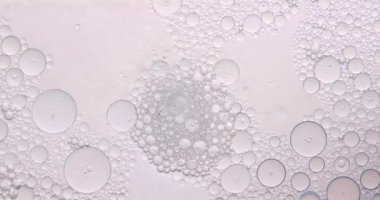 Yumuşak, soyut güzellik arka planında, temiz bir kozmetik dokusu yaratmak için hafif ışıkla aydınlatılmış, berrak sıvı içinde yüzen yağ kabarcıkları var. Yavaş çekim.