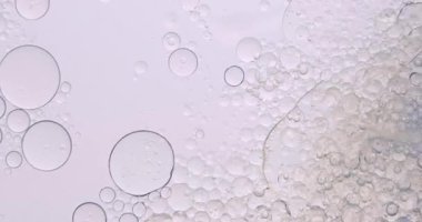 Yumuşak, soyut güzellik arka planında, temiz bir kozmetik dokusu yaratmak için hafif ışıkla aydınlatılmış, berrak sıvı içinde yüzen yağ kabarcıkları var. Yavaş çekim.
