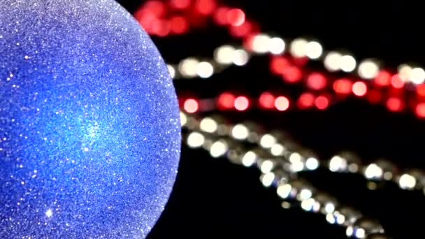 Синяя игрушка на Рождество или Новый год и бусы, вращение, на красном и зеленом, крупным планом — стоковое видео