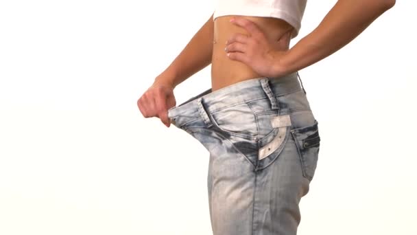 Schlanke Mädchen in großen Jeans, zeigt ihr Gewicht zu verlieren und dreht sich auf weiß — Stockvideo