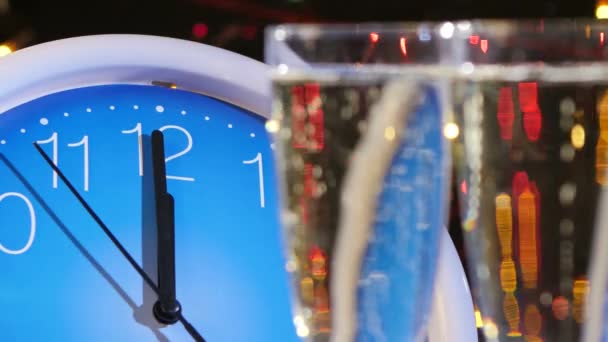 La cima di occhiali con champagne durante Vigilia di anno nuovo contro orologio di parete, bokeh, ghirlanda, su nero, camma si muove a sinistra, da vicino — Video Stock