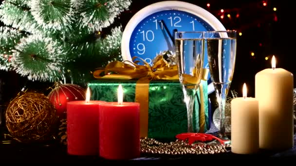 Naléval šampaňské na nový rok večer proti nástěnné hodiny, svíčky, dárky, bokeh, věnec, na černou, kamera se pohybuje doprava — Stock video