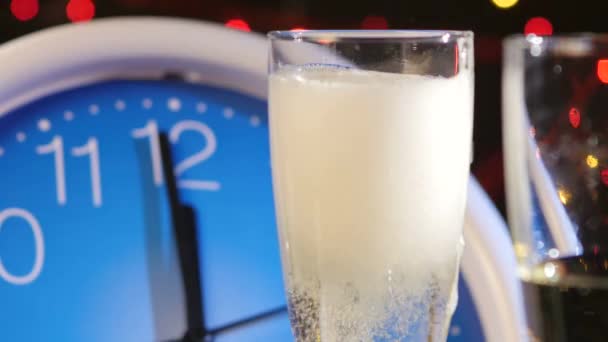 Lití bublina šampaňské do sklenic na nový rok večer proti nástěnné hodiny, bokeh, věnec, na černou, blízko nahoru — Stock video