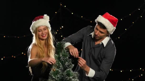 Bella coppia in cappelli di Natale decorare un albero di Natale su nero — Video Stock