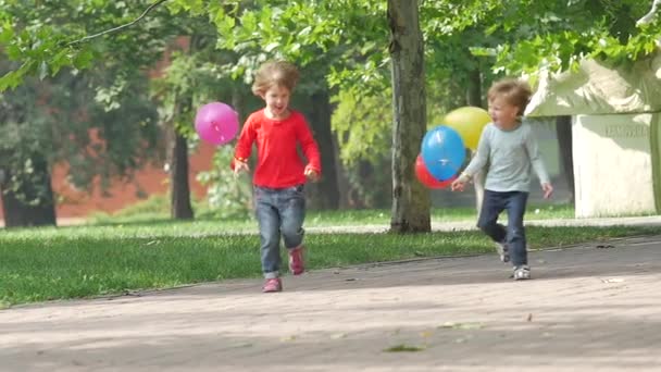 Smějící se dvě malé sestry s balónky v parku, pomalý pohyb