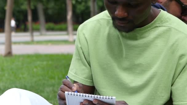 African-American man writes in a notebook at the park, slow motion — Stock Video