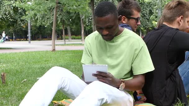 Афроамериканец пишет в блокноте в парке, замедленная съемка — стоковое видео