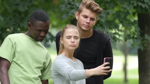 Amigos felices tomando una selfie en un cielo azul en el césped del campus, hombre africano. cámara lenta — Vídeos de Stock