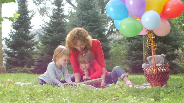 Счастливые мама и дочь читают книгу в парке — стоковое видео