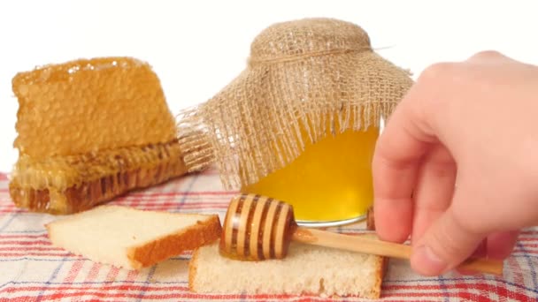 Gotejador de colher de mel e frasco com vara derramando sobre pão torrado, favo de mel em branco — Vídeo de Stock