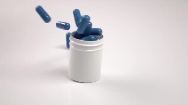 Pilule bouteille avec des pilules bleues tombant vers le bas, sur blanc, gros plan, ralenti — Video