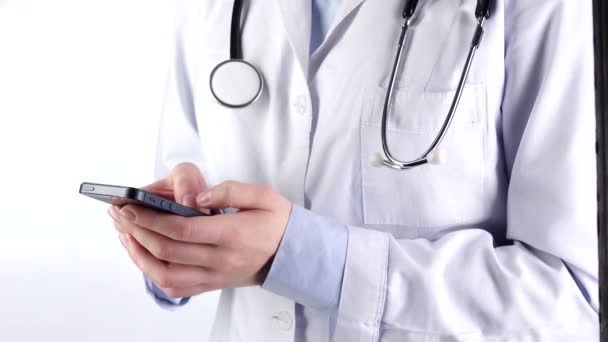 Γιατρός στέκεται, κρατώντας και πληκτρολογώντας στο κινητό τηλέφωνο, φορώντας στηθοσκόπιο, λευκό — Αρχείο Βίντεο