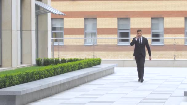 Hombre de negocios hablando por teléfono mientras camina por el edificio moderno — Vídeo de stock