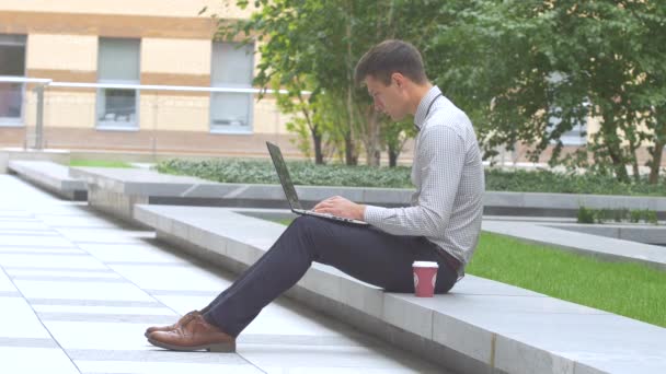 Hombre elegante que trabaja en el ordenador portátil al aire libre, terraza, taza de café — Vídeo de stock