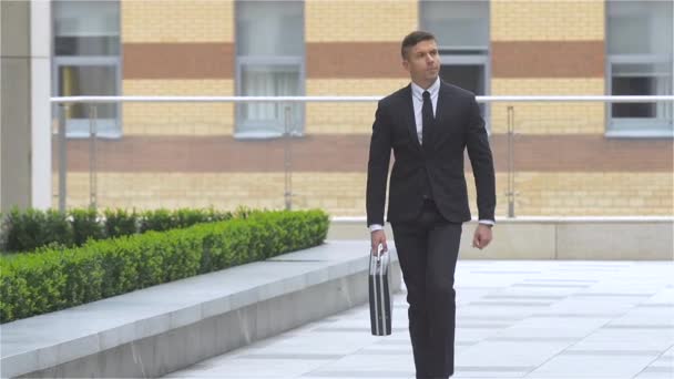 Attractive businessman with a suitcase goes around the building, slow motion — Stock Video