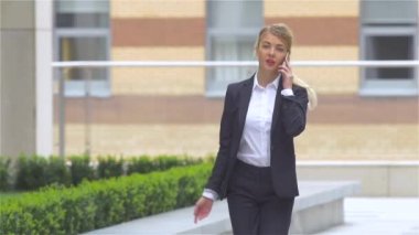 Başarılı sarışın kadın açık havada yürürken cep telefonukonuşuyor. yavaş çekim