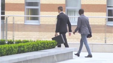 Ofis binasının yanındaki sokakta yürüyen iki işadamı. yavaş çekim