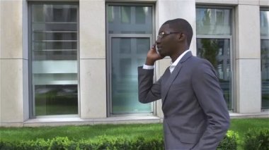 Amerikalı işadamı cep telefonuyla konuşuyor, ofisinin önünde duruyor. yavaş çekim