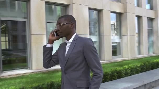 Un homme d'affaires afro-américain parlant sur son portable, debout devant son bureau. au ralenti — Video