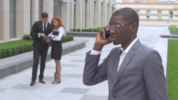 Boldog többnemzetiségű üzletemberek csoportja. Afro-amerikai beszél a telefonon — Stock videók