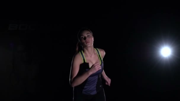 Фитнес-женщина начинает выбегать из темноты в спортзале, замедленная съемка — стоковое видео