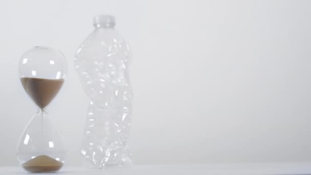 Szerokie Ujęcie Studyjne Zmiażdżonej Plastikowej Butelki Jednorazowego Użytku Obok Zegara — Wideo stockowe