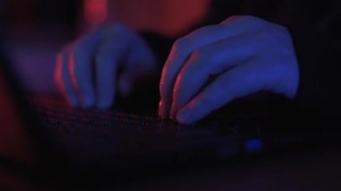 Renkli ama loş bir odada klavyeye yazı yazan isimsiz bir hacker 'ın ellerini kapat.