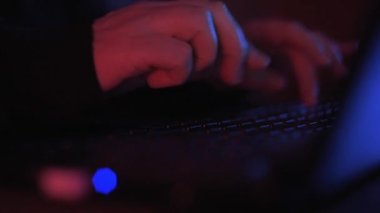 Renkli ama loş bir odada klavyeye yazı yazan isimsiz bir hacker 'ın ellerini kapat.