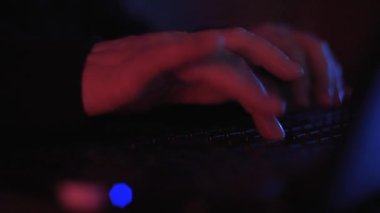 Renkli ama loş bir odada klavyeye yazı yazan isimsiz bir hacker 'ın ellerini kapat.