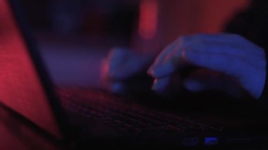Renkli ama loş bir odada klavyeye yazı yazan isimsiz bir hacker 'ın ellerini kapat.