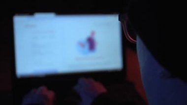 Karanlık bir odada dizüstü bilgisayar kullanan bir kadın hacker 'ın omuz hizasında yakın bir el kamerası.
