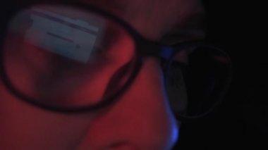 Dişi bir hacker 'ın gözlüklerine yansıyan dizüstü bilgisayarın yakın el kamerası görüntüsü.
