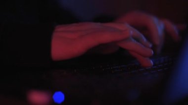 Renkli ama loş bir odada klavyeye yazı yazan isimsiz bir hacker 'ın ellerini kapat.