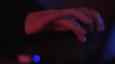 Renkli ama loş bir odada klavyeye yazı yazan isimsiz bir hacker 'ın ellerini kapat.