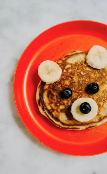 Pancakes on plate with fruits in shape on teddy bear. Childhood breakfast, lunch
