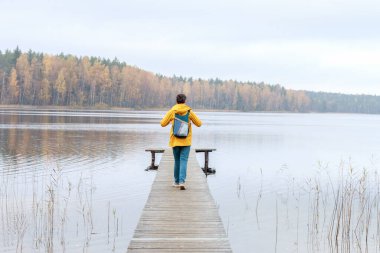 Bir sonbahar günü, bir göldeki ahşap iskelede yürüyen bir adam. 