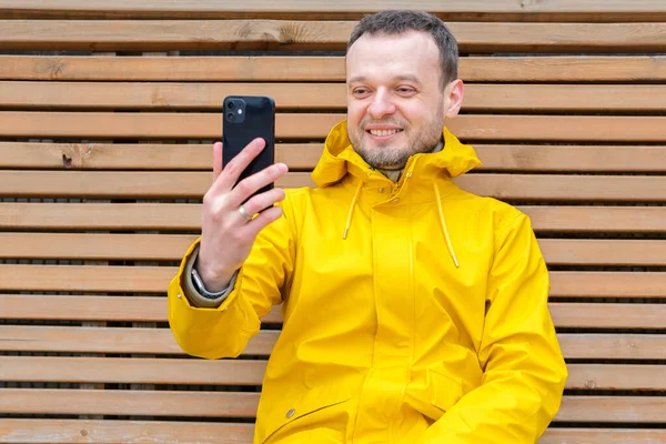 Счастливый человек сидит снаружи и смотрит и улыбается на телефон Лицензионные Стоковые Изображения