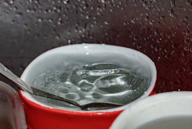 Bulaşık lavabosunda kaşıkla bardağa su dökülüyor.