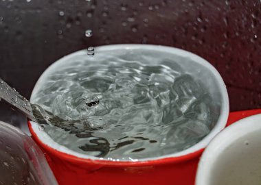 Bulaşık lavabosunda kaşıkla bardağa su dökülüyor.