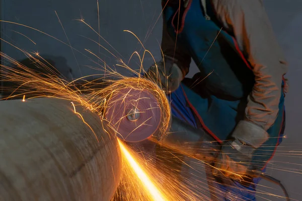 Manufacturing of steel pipes in one of the plant\'s workshops. Rotation of the angle grinder disc during operation. Bright sparks from metal cutting. Preparation of metal structures before welding.