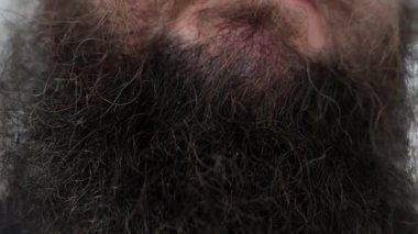 Detaylı bir yakın çekim, bir adamın kalın, koyu ve kırpılmamış sakalının doğal gelişimine odaklanır. Yüz kıllarının karmaşık dokusu ve renk varyasyonları sert erkekliğin ve doğal tımarın altını çiziyor..