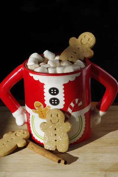 three gingerbread  smiley face cookies in a funny Mrs. Santa Clause coffee mug with hot chocolate, marshmallows
