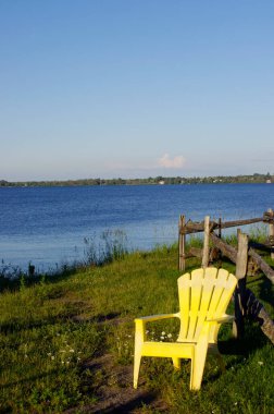 Su kenarında parlak sarı Adirondack sandalyesi mavi gökyüzü kopyalama alanı