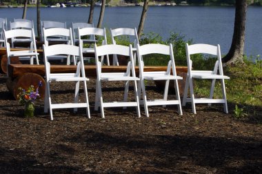 Beyaz ahşap düğün sandalyeleri dışarıda, doğada suyla birlikte.